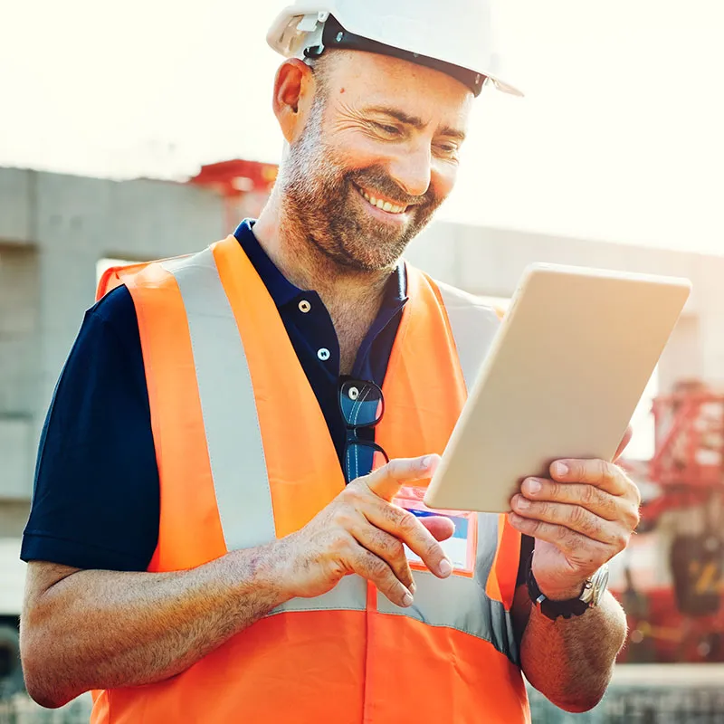 Site engineer in a hard hat and high-visibility vest smiling at a tablet