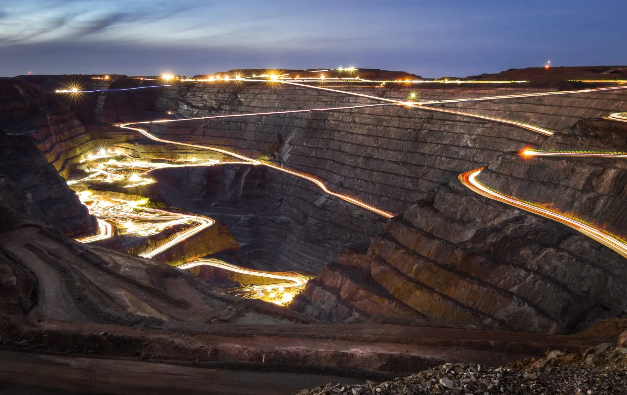 Open pit gold mine lit up at dusk with haul roads traced by vehicle lights